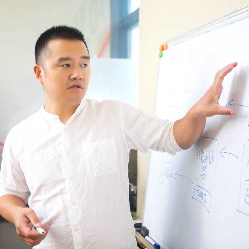A senior engineer explaining a system design at a whiteboard